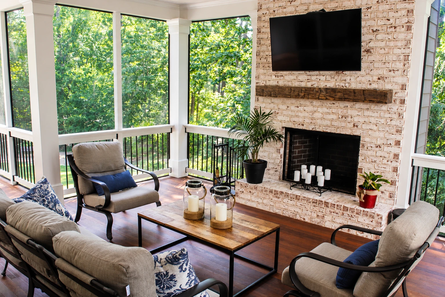 A bright enclosed deck serves as a sitting room, with large windows, cushioned chairs, a brick fireplace and a wall-mounted television.