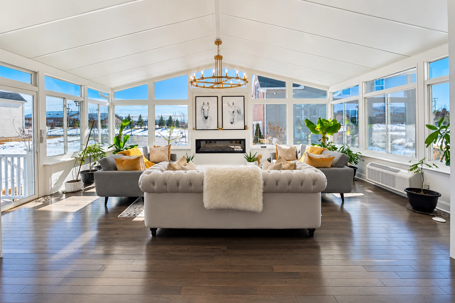 Four-season sunroom with white-framed windows, a vaulted ceiling, sofas, a chandelier, and snow outside.