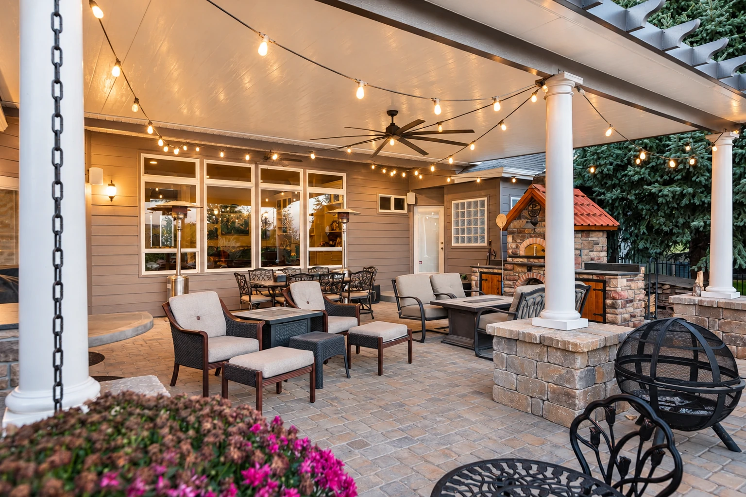 A covered patio with white columns, string lights, outdoor seating, and a brick oven.