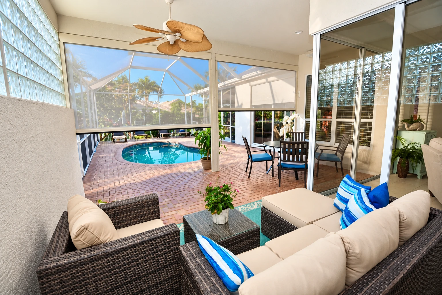 A screened patio room overlooks a swimming pool, with wicker lounge seating, sliding glass doors and a ceiling fan.