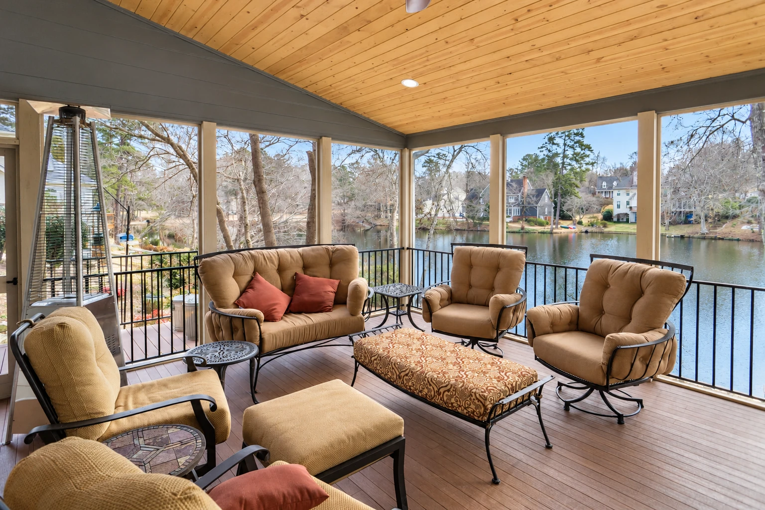 A furnished screened sunroom has a wood-paneled ceiling, cushioned chairs and broad views across a lake.