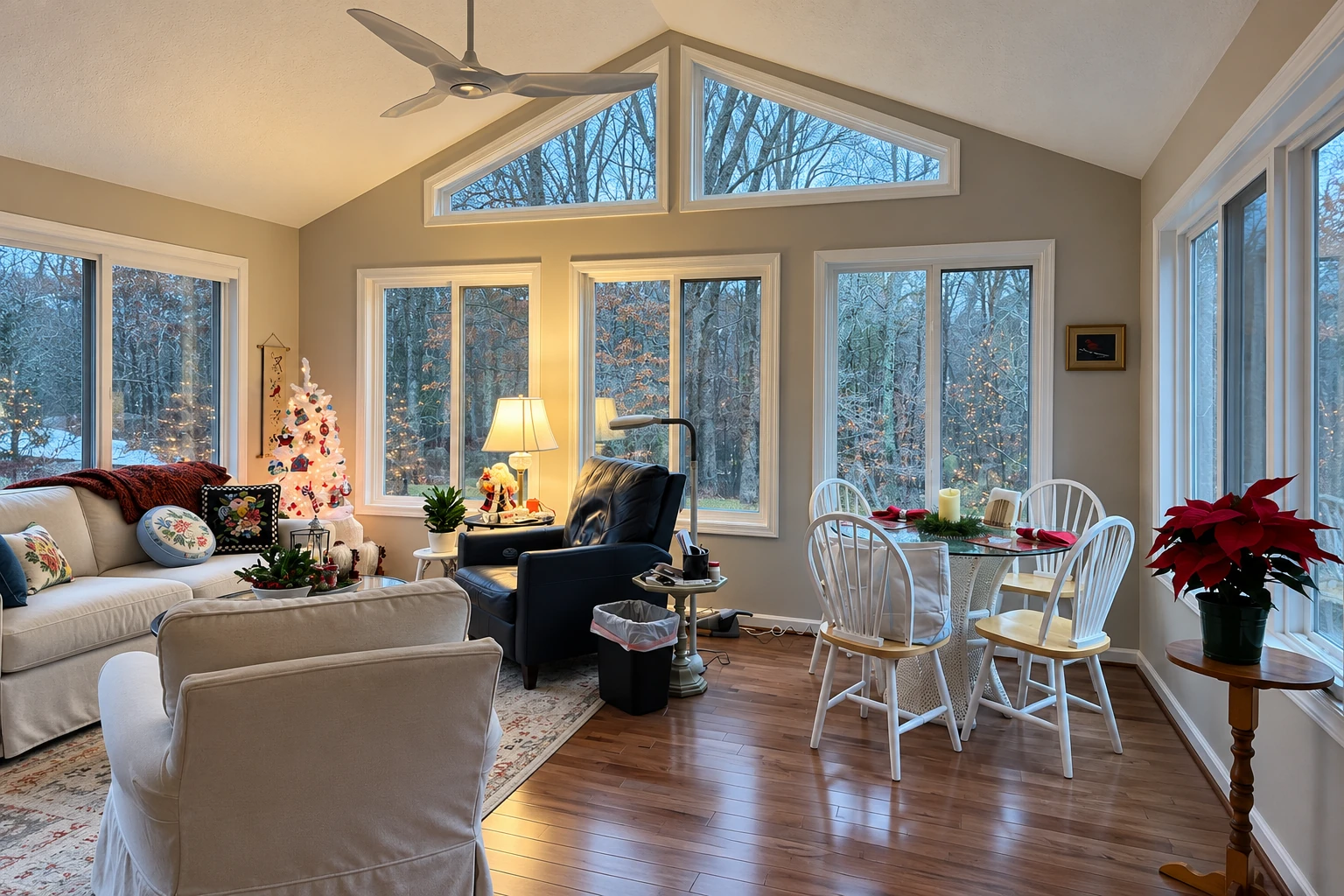 Sunroom with a high ceiling, large windows, seating and dining areas, and a small decorated Christmas tree.